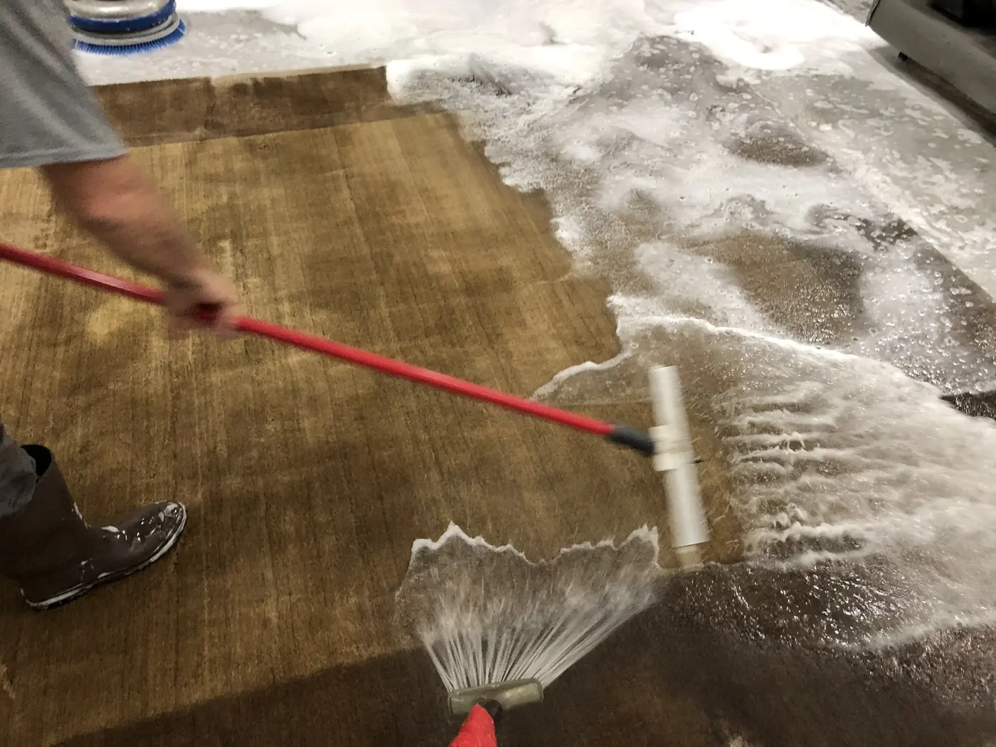 Rinsing a large rug with a wand on the wash floor
